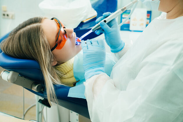 肖像一个戴着眼镜的年轻漂亮女孩在牙医那里用紫外线治疗牙齿补牙灯医生医学