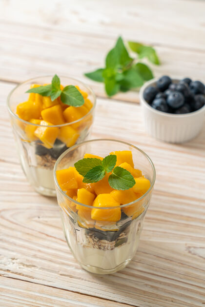 薄荷自制新鲜芒果和新鲜蓝莓配酸奶和格兰诺拉麦片-健康食品风格餐桌零食碗