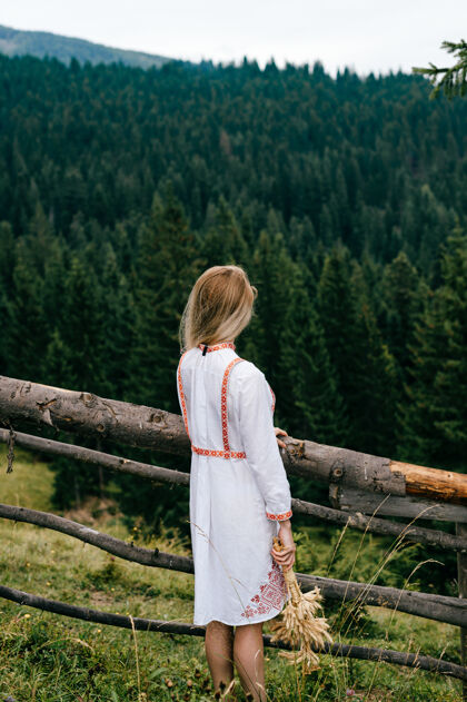 年轻年轻迷人的金发女孩 穿着白色刺绣裙 在风景如画的木栅栏旁摆着小穗花束夏天乡村女人