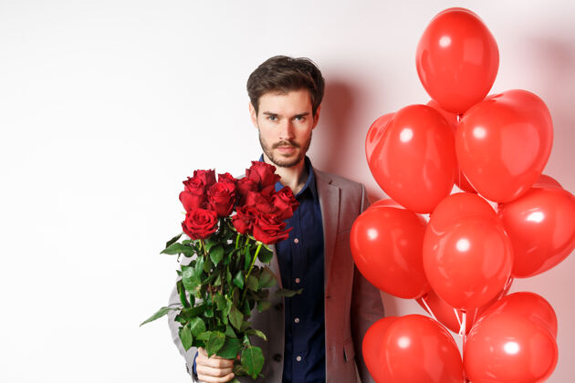 男人男子汉在浪漫的约会 自信的看着镜头 在情人节拿着礼物 站着心形气球和红玫瑰 白色的背景感情微笑丈夫