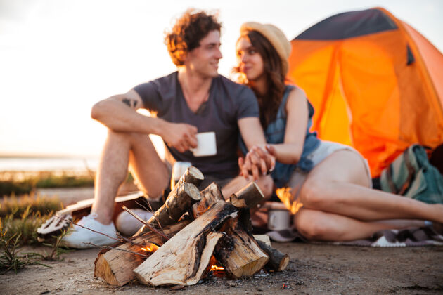 男朋友年轻幸福的一对在篝火边喝茶 露营时互相看着对方举行自然度假