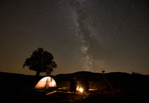 旅游两位游客在帐篷前燃起营火 在漆黑的星空下用三脚架拍照剪影设备休闲