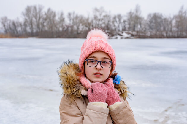 年轻戴着粉色帽子和外套的少女站在冬天风景中的肖像戴眼镜的可爱女孩快乐寒冷帽子