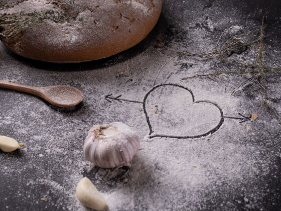 烘焙在自制蒜蓉面包和调味品旁边的灰色桌子上 心被画在面粉上情人节面团准备