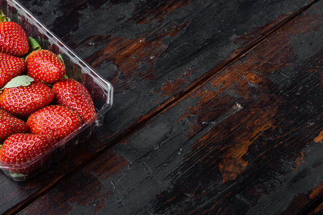 木桌红色成熟的草莓放在透明的塑料托盘里 放在旧的深色木桌上浆果顶视图甜点