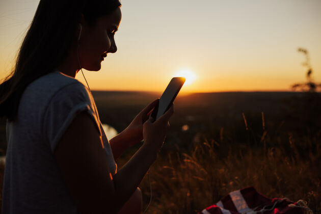 华丽特写镜头和侧视图的妇女使用手机在美丽的日落美丽时间坐着
