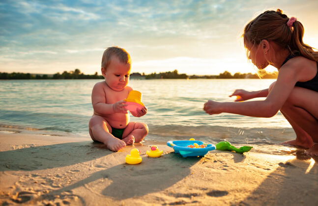 玩侧视图：可爱的小宝宝和小橡皮黄鸭子在蓝色的小水池里玩耍 和姐姐坐在沙滩上童年一起海滩