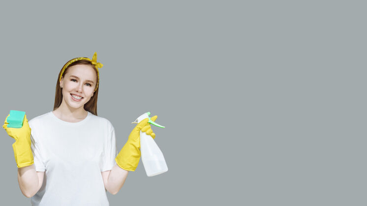 肖像年轻的家庭主妇戴着黄色手套 带着清洁喷雾和海绵微笑橡皮手套女仆