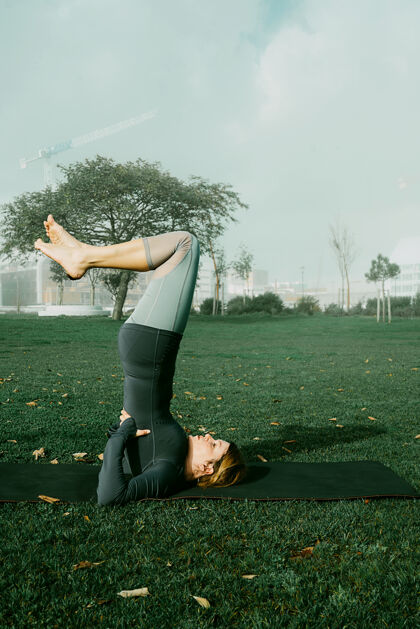 运动在公园里用瑜伽垫做瑜伽 伸展运动 锻炼的年轻女子天生的瑜伽初学者姿势医疗理念公园户外运动