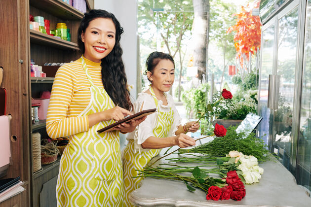 工作快乐的越南年轻花店老板在花店制作花束时 通过数字平板电脑上的应用程序回答顾客的问题接受小企业亚洲