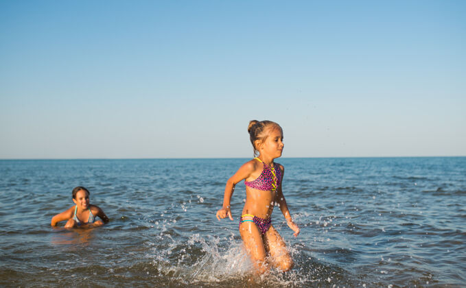 享受在一个阳光明媚的炎炎夏日 两个快乐而积极的女孩姐妹在度假时沿着海浪奔跑年轻泡沫活跃