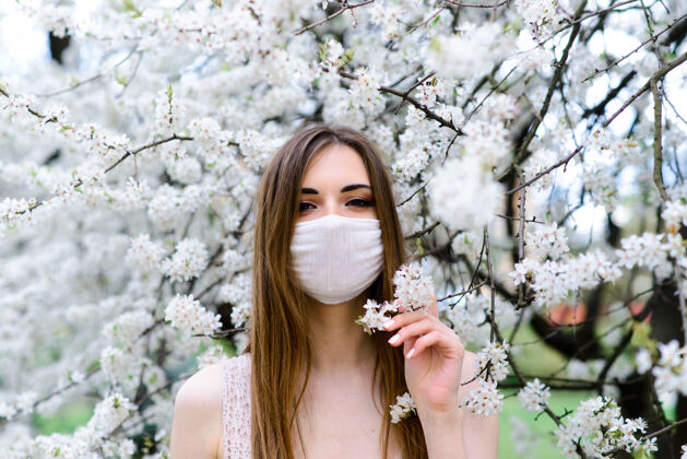 健康在樱花盛开的樱花树下 一个穿着白色上衣 戴着冠状病毒花朵面具的温柔女孩的特写镜头流行病检疫花