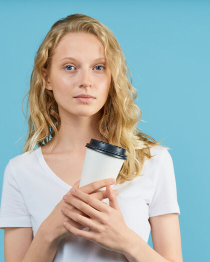 女性在中性色调的蓝色墙上 年轻女学生拿着一杯咖啡的画像长发肖像严肃