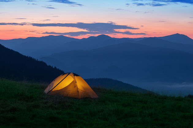 设备橙色的旅游帐篷从内部照亮山早早晨或日落徒步旅行户外冒险