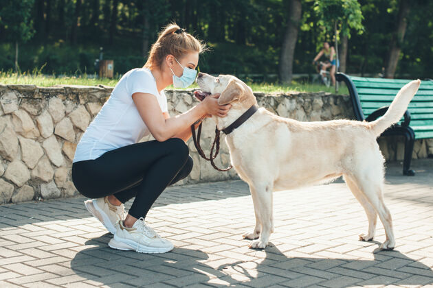 爱情一位戴着医用面具的白人妇女在公园散步时拥抱她的金毛猎犬的侧视照片活跃自然生活方式