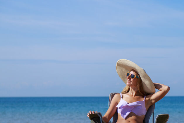 头去天堂的旅程海上女孩穿着泳衣戴着帽子在沙滩上晒太阳海滩旅游者坐在桌子上沙滩休闲磨损复制空间日光浴海洋假日