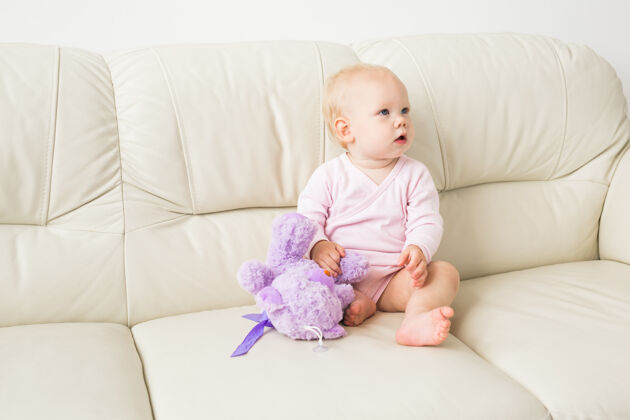 房子童年 婴儿期和人的概念-快乐的小女婴坐在家里的沙发上婴儿期年轻尿布