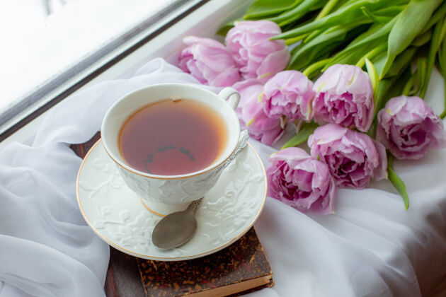 白色床单一杯茶一本旧书一束郁金香在窗户上花束甜粉色郁金香