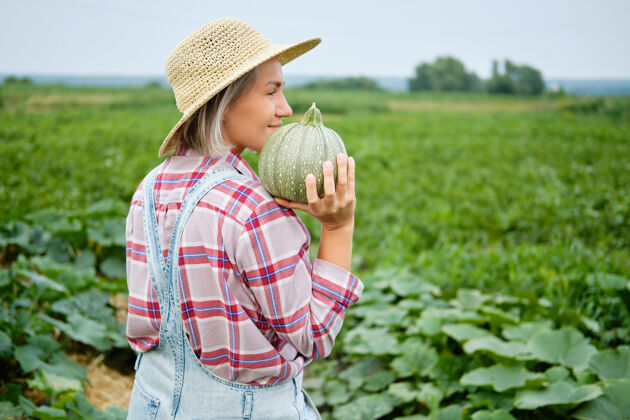 田地在植物上拿着新鲜绿色南瓜的女人田野美丽在阳光明媚的温暖天气里 一个拿着健康蔬菜食品的小女孩站在农场上日间栽培纯素文化有机自然产品膳食温暖帽子