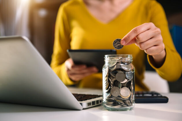 商业女商人拿着硬币放在玻璃里 用智能手机和计算器计算概念 为财务会计省钱银行储蓄增长