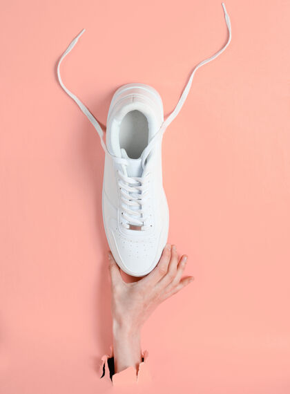 商店女性手拿白色运动鞋穿过撕破的粉色纸简约创意时尚理念青少年运动创意