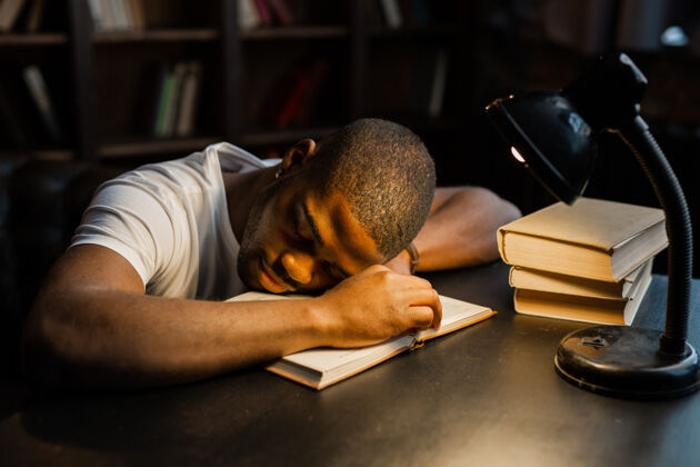 大学帅气的非洲年轻人拿着书睡在桌子上人非洲休闲