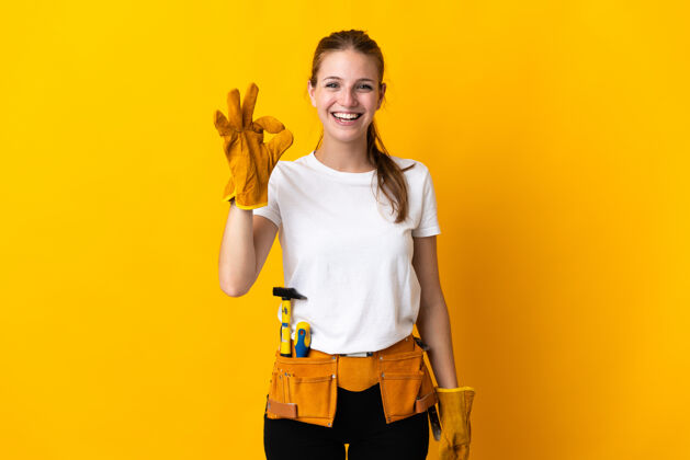Ok在黄色背景上被隔离的年轻电工女士用手指显示ok标志工作修理车间