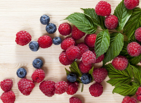 叶子 成熟的覆盆子和多汁的蓝莓放在木板上 红色的覆盆子被叶子覆盖着 夏天特写水果特写黑莓