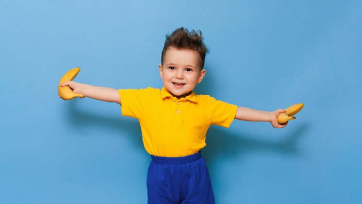 童年一个穿黄色t恤衫的男孩手里拿着一根香蕉和一只手微笑有趣表达肖像快乐素食