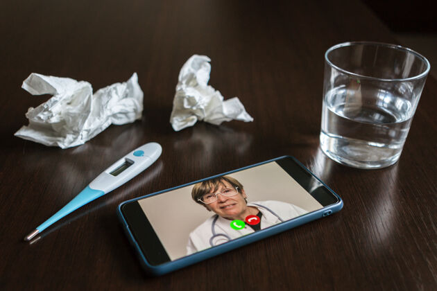 医疗手机屏幕上有一位男性医生在线 一些纸巾 一杯水和温度表放在桌子上工作医院健康