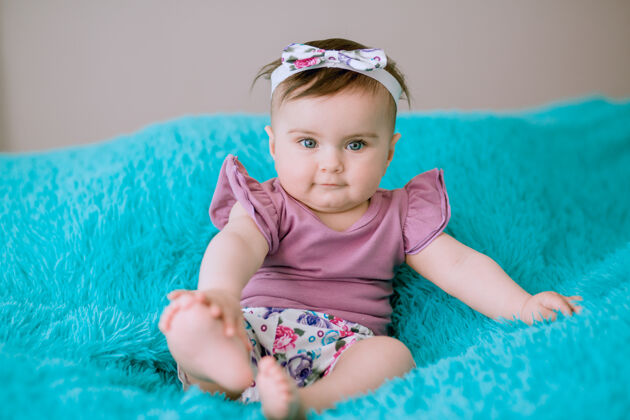房间六个月大的婴儿头上戴着创意丝带坐在床上看着相机婴儿小宝贝