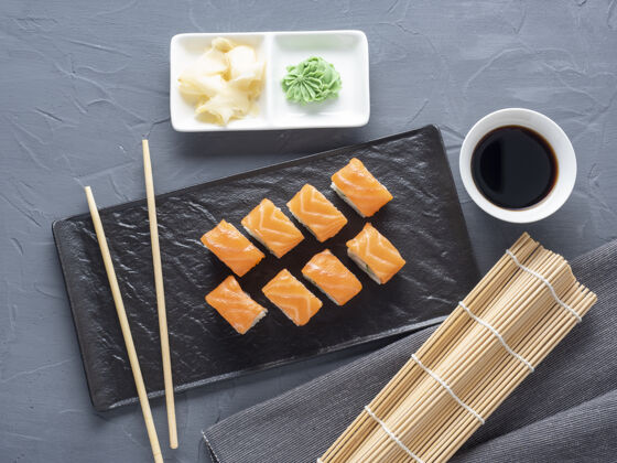 生的费城寿司卷放在一个黑色纹理的盘子里 放在一个灰色的架子上背景.top视图 平面日语美食加州奶酪什锦