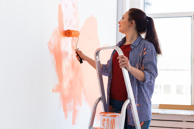 人快乐的年轻女子在新房子里用油漆辊粉刷内墙承包商职业举行