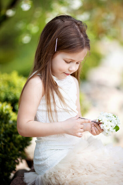 草地美丽微笑的小女孩穿着奶油色的裙子 映衬着夏日公园的绿色草年轻快乐