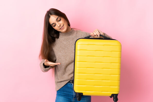 提手年轻的白种女人带着旅行箱在度假时被隔离在粉色背景下行李黑发成人