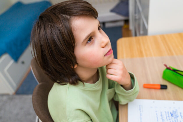 房间小男孩坐在桌子旁做作业家集中思考任务的孩子兴趣.家庭教育教育钢笔桌子教育