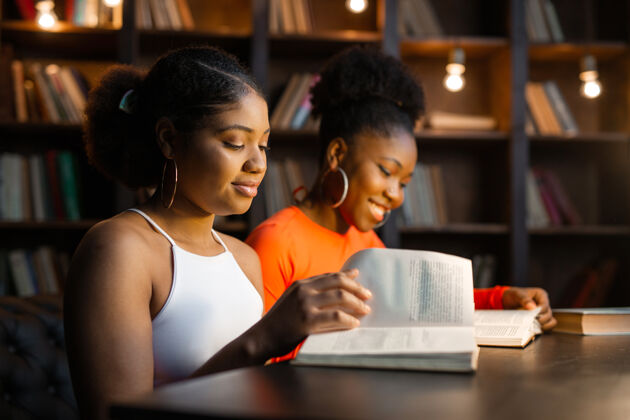 大学两个年轻的非洲女人在图书馆看书微笑民族人