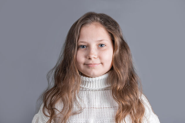 自然一个年轻漂亮的小女孩的肖像 金发飘逸 穿着白色毛衣 在灰色的工作室里微笑背景.地点为了文本.复制空间肖像看欢呼