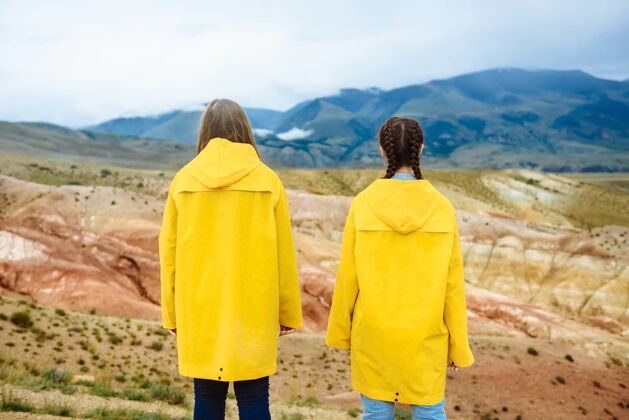 举行两个女孩远足者在看彩色山脉的照片旅行者人自然