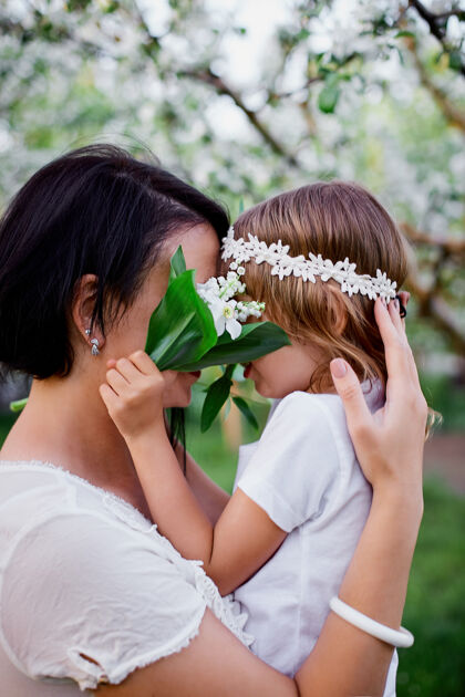 户外可爱的女儿和妈妈在花泉花园拥抱孩子年轻拥抱
