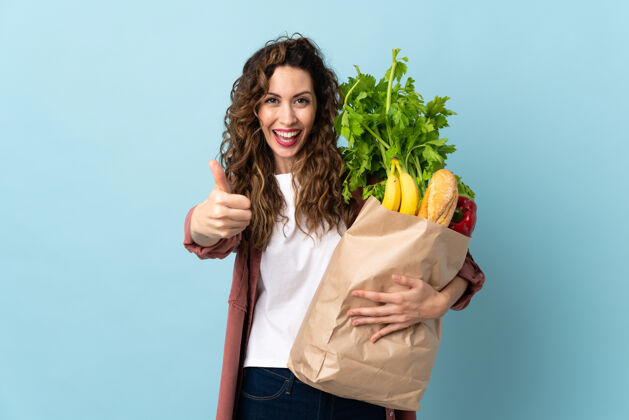 蔬菜一个年轻的女人拿着一个杂货店的购物袋 因为发生了什么好事 她竖起了大拇指食物女性购买
