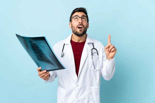 诊断专业的创伤科医生拿着蓝色背景上孤立的X光片用食指指着是个好主意信心健康指点