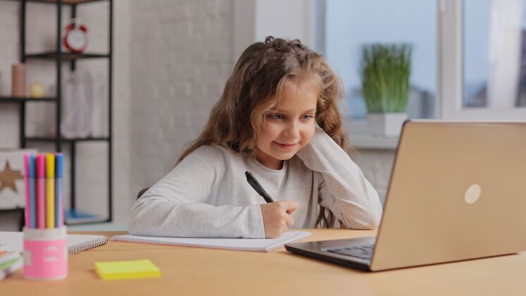 女孩可爱的小学生在家用笔记本电脑学习电脑女学生有在线课程讲座家庭作业课程