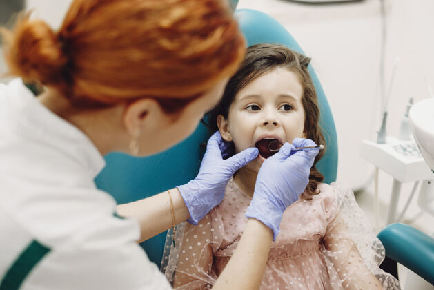 医生一个可爱的小女孩坐在口腔科的座位上 接受儿科口腔医生的牙齿检查初级红发药品