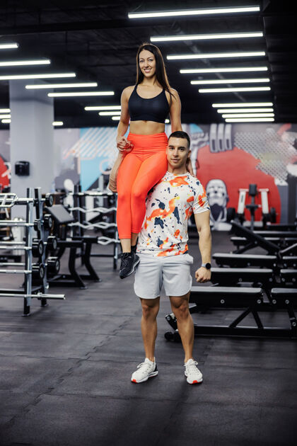 团队合作强壮的运动员把女人扛在肩上 摆出姿势健身 健活运动运动装健身房