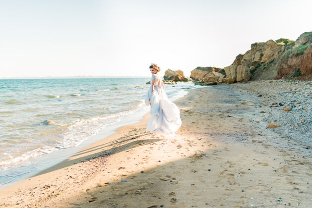 时尚幸福的深褐色新娘在轻雪纺婚纱绣珠摆在海边度假新娘优雅