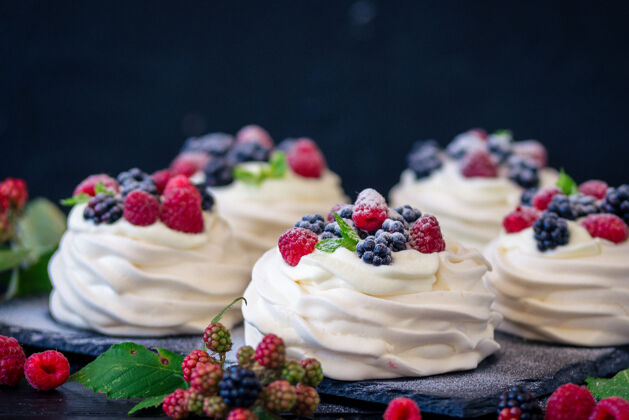 蛋白酥皮巴甫洛娃蛋糕的自制蛋白酥皮 配以新鲜蓝莓 黑莓和糖粉 表面为黑色混凝土纹理年份蛋糕奶油