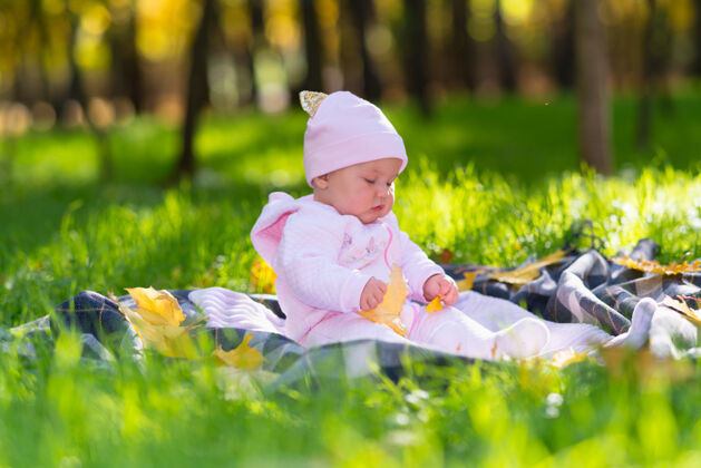 树叶在秋天的森林空地上 一个心满意足的小女婴在草地上的毯子上玩黄叶婴儿新生儿抬头