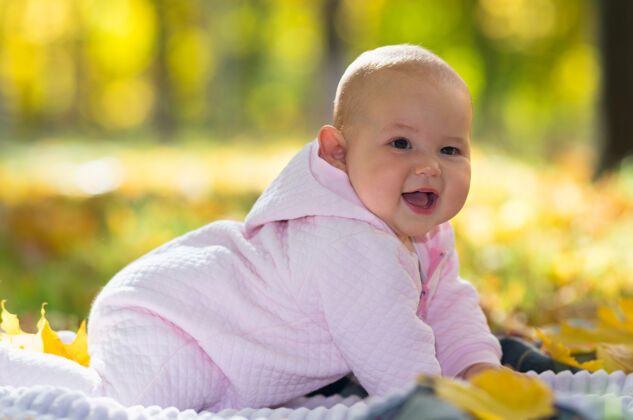 童年可爱的胖乎乎的小女婴在相机前笑着 她在草地上的地毯上爬行 在一个秋天的公园可爱玩耍女孩