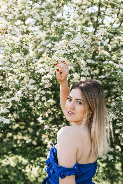 女孩美丽的时髦女人在盛开的灌木中的感性平静的肖像 白色的花朵绣线菊空间时尚花园里穿着蓝色裙子的金发女人光自然户外